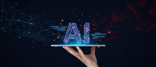 Das Bild zeigt eine Hand, die auf einem Tablet das Wort "AI" darstellt.