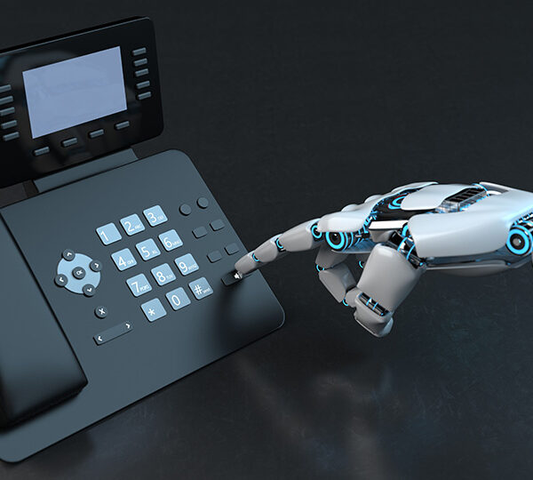 Das Bild zeigt einen modernen Schreibtischtelefonapparat, der von einem Roboterarm bedient wird.