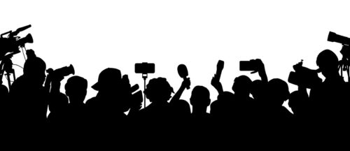 Bildbeschreibung: Das Bild zeigt die Silhouetten einer Gruppe von Medienvertretern, darunter Fotografen und Reporter, die Kameras und Mikrofone halten, vermutlich bei einer Pressekonferenz oder einem ähnlichen Ereignis.