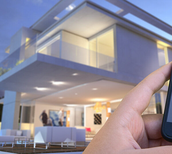 Das Bild zeigt eine Hand, die ein Smartphone mit einer Smart-Home-App bedient, durch welche die Sicherheitssysteme eines modernen, gut beleuchteten Hauses im Abendlicht kontrolliert werden.