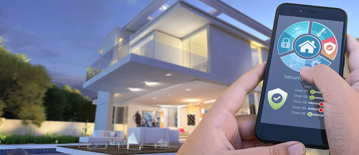 Das Bild zeigt eine Hand, die ein Smartphone mit einer Smart-Home-App bedient, durch welche die Sicherheitssysteme eines modernen, gut beleuchteten Hauses im Abendlicht kontrolliert werden.