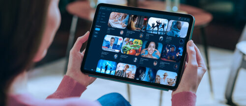 Im Bild ist eine Person zu sehen, die ein Tablet hält und darauf eine Streaming-App mit verschiedenen Film-vorschlägen benutzt.